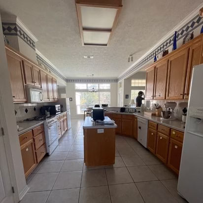 Original kitchen before an aging in place whole home remodel featuring oak cabinetry, tile flooring, center island, and builder-grade lighting prior to renovation.