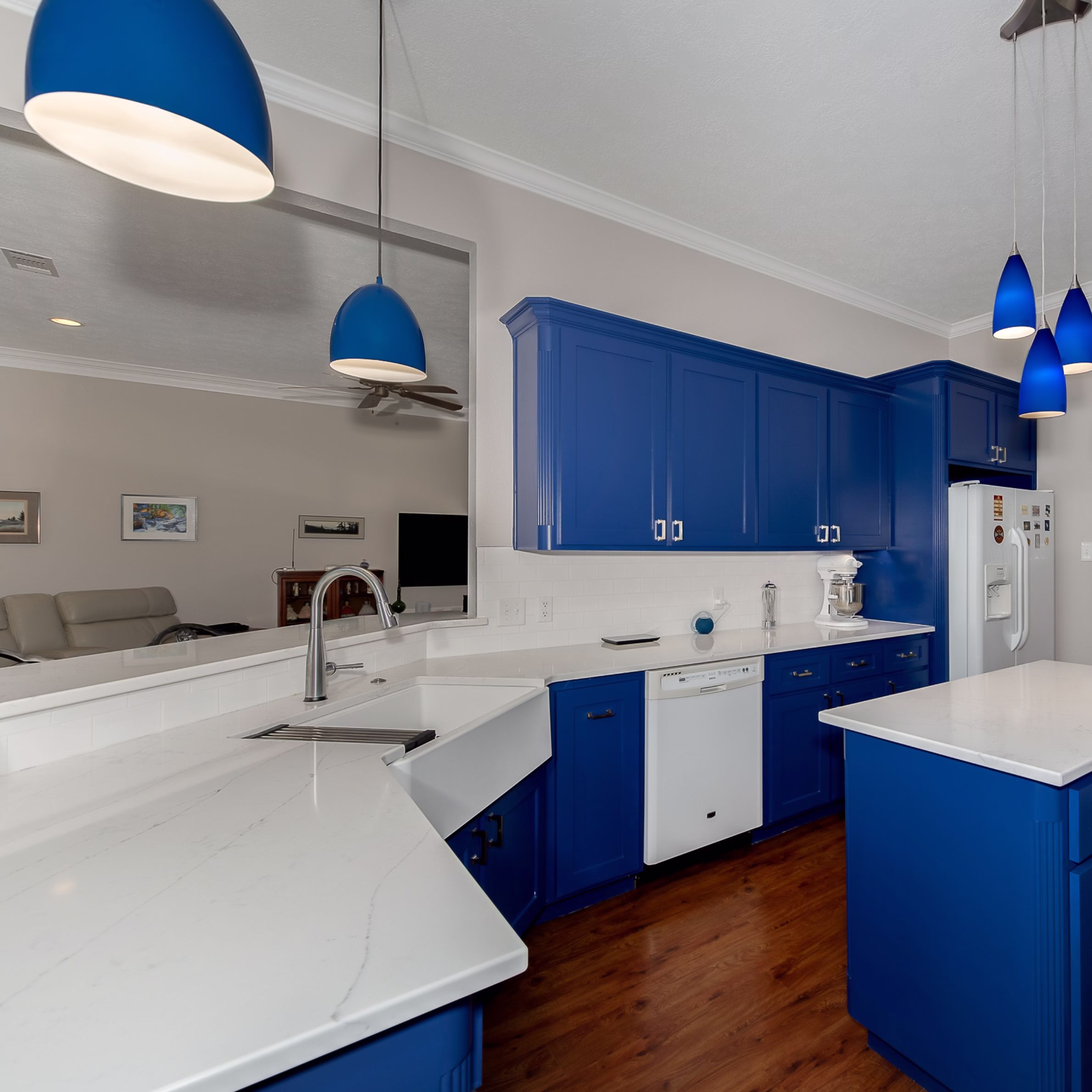 Bright kitchen featuring cobalt blue cabinetry, workstation apron-front sink, quartz countertops, and new pendant lighting as part of an aging in place remodel.