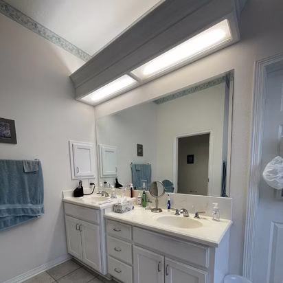 Original double vanity in a whole home renovation Bryan TX project showing dated lighting, cultured marble countertops, and traditional cabinetry before remodeling.