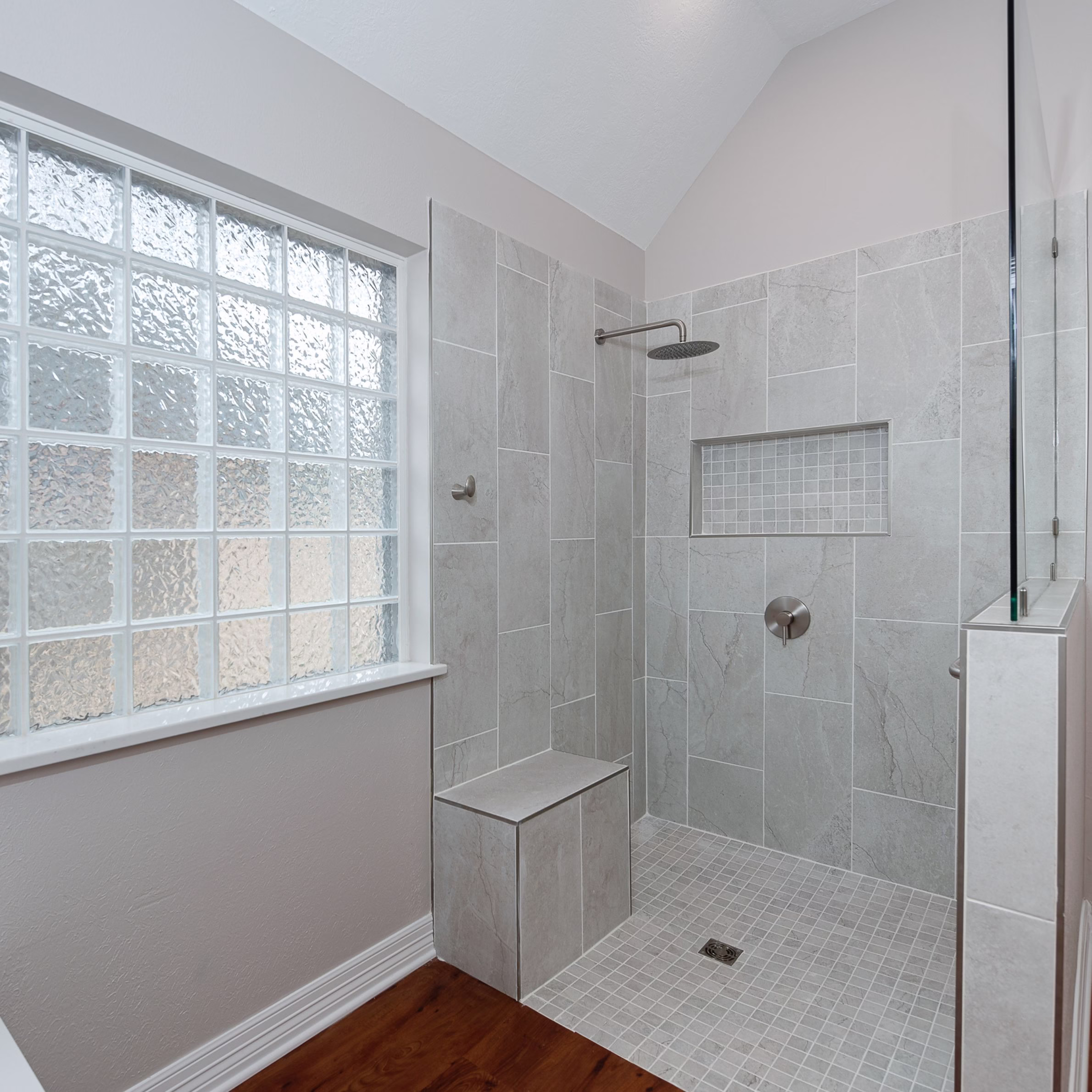 Curbless walk-in shower with integrated bench, grab bar, tiled niche, and frameless glass enclosure completed during an accessible bathroom remodel supporting aging in place.