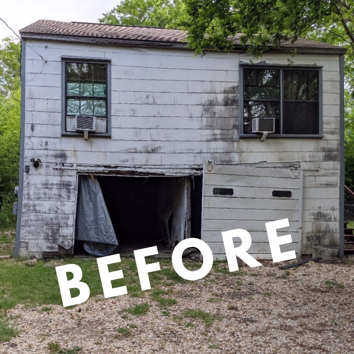 Rear of an older two-story guest house showing weathered siding and damaged garage doors before renovation