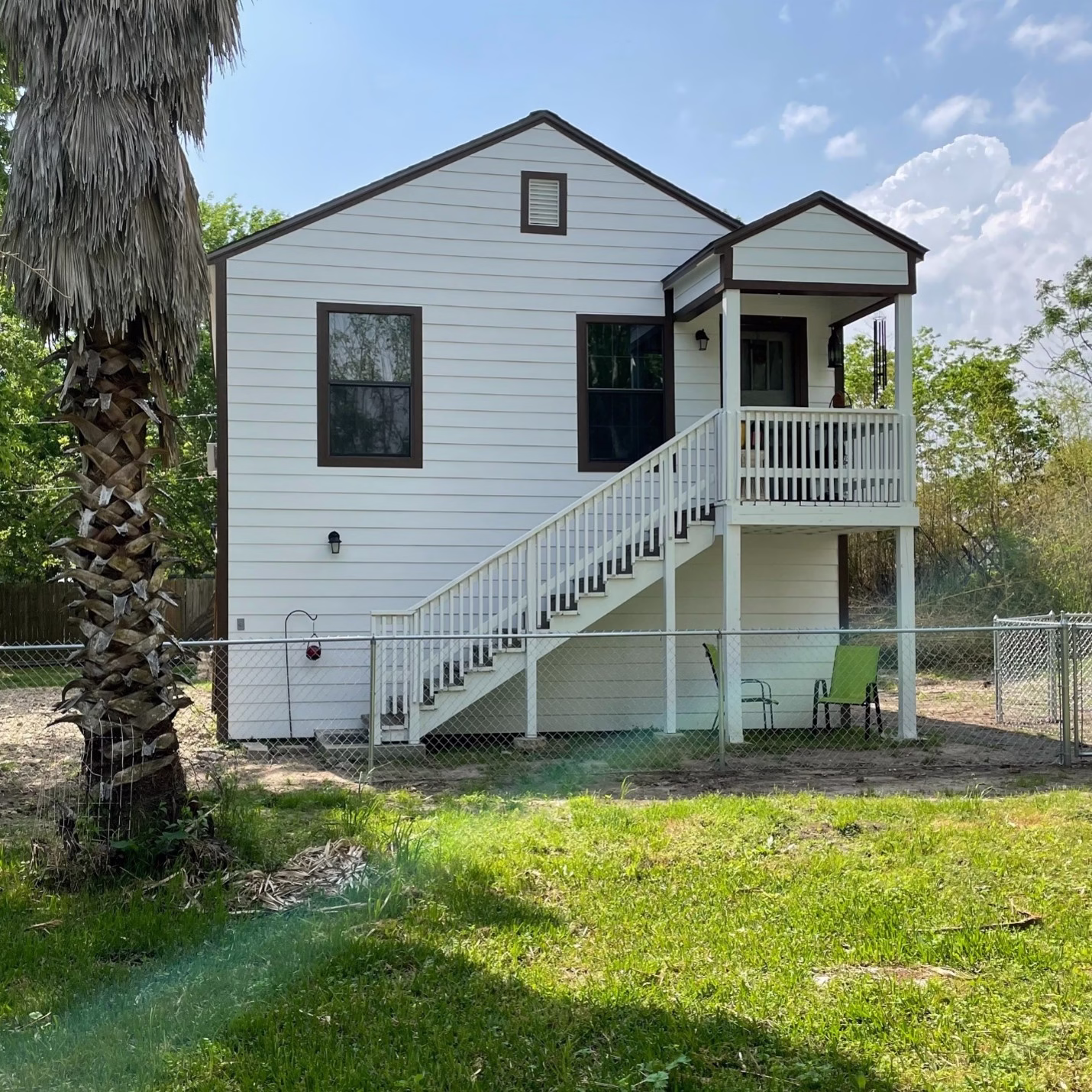 Front view of the restored guest house with white siding, dark trim, and a rebuilt staircase leading to the covered upper porch