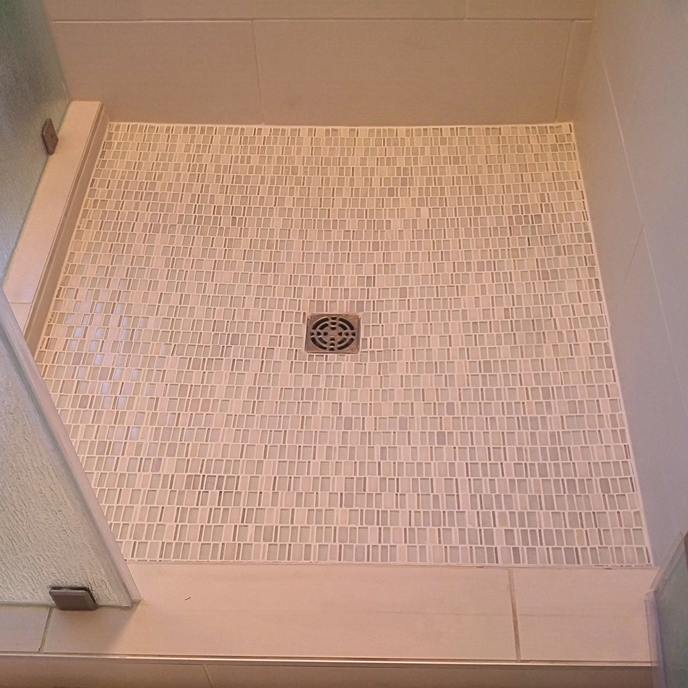 White mosaic tile shower floor with centered drain, large-format wall tile, and glass shower enclosure.