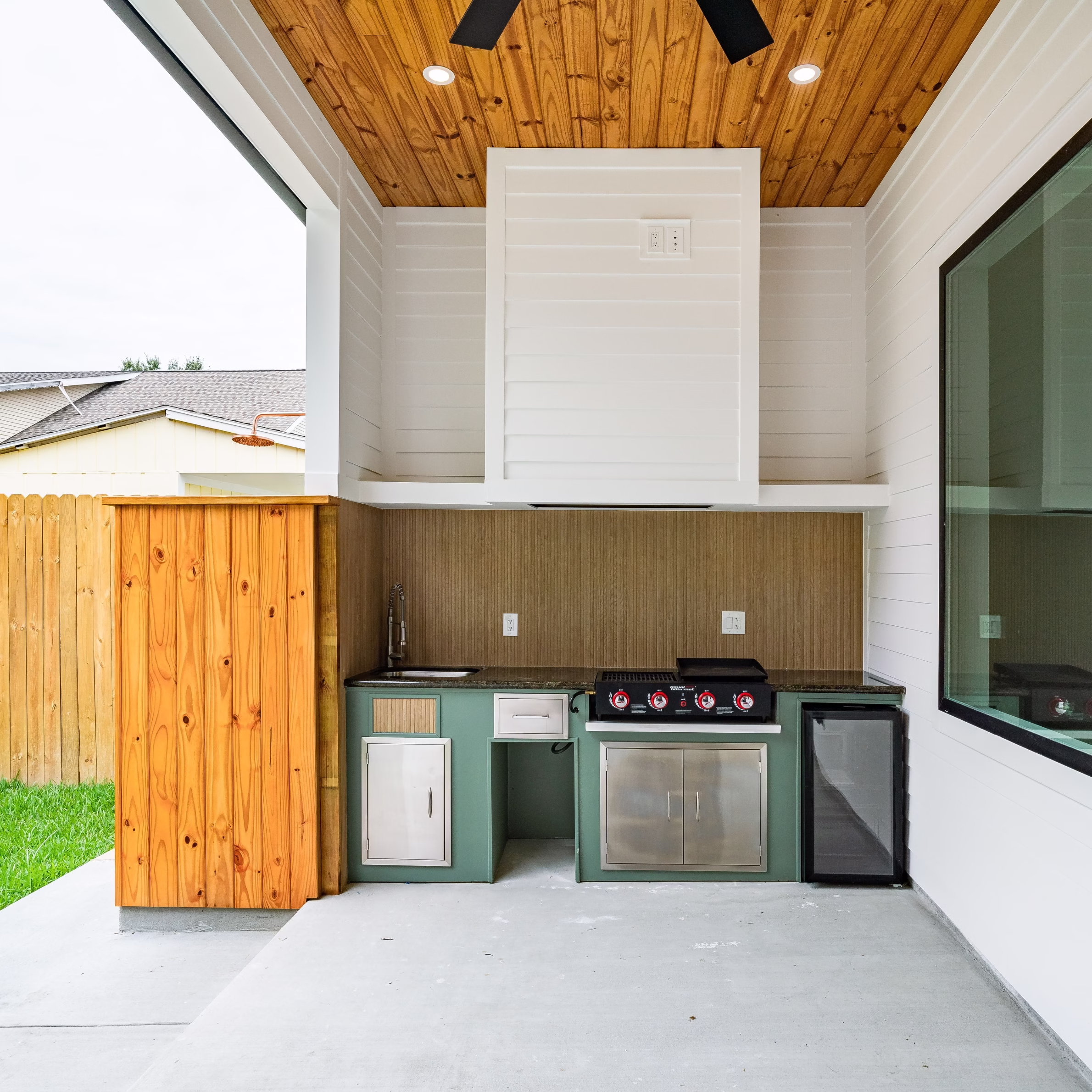 Covered outdoor kitchen with built-in grill, sink, mini refrigerator, and green cabinetry.