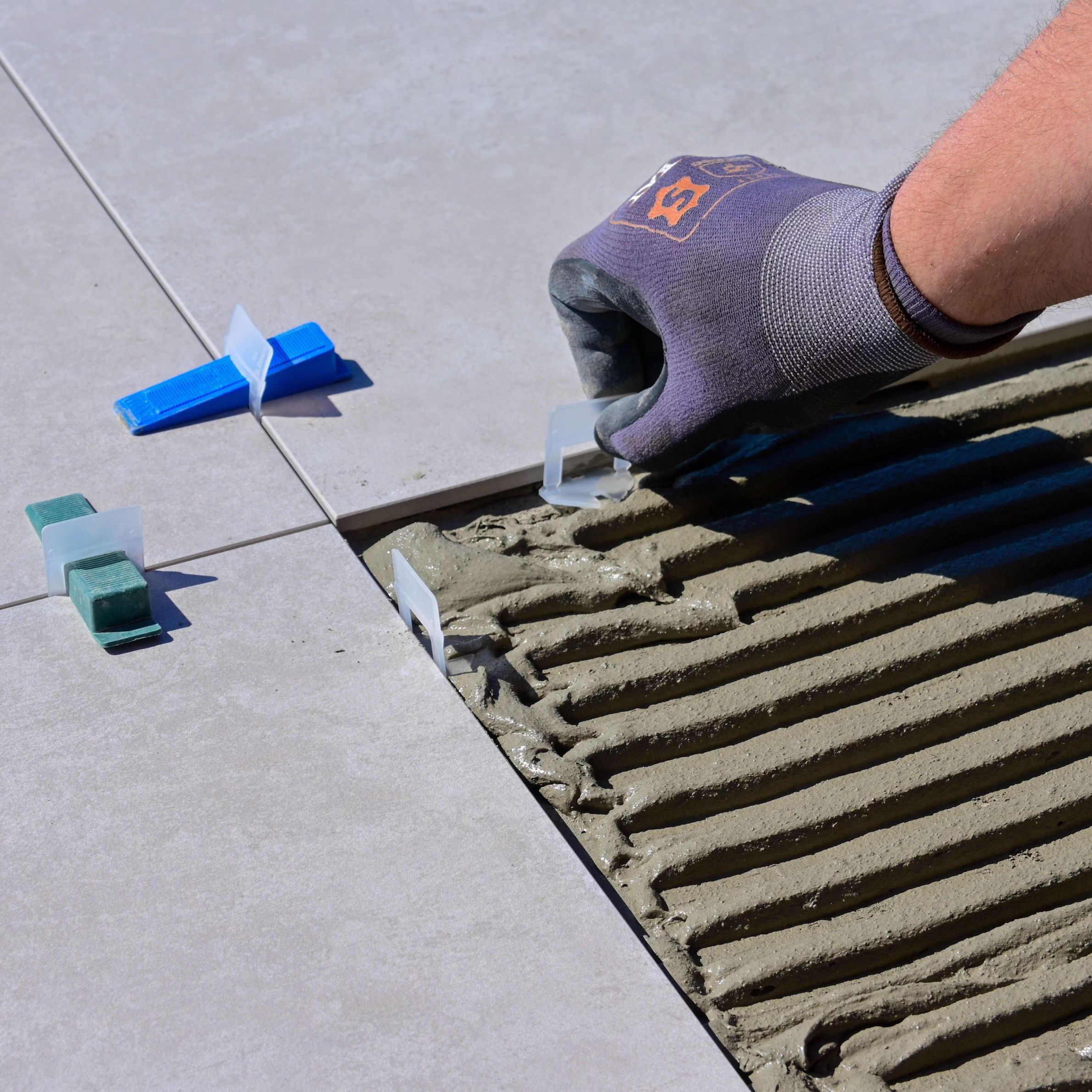 Large-format floor tile being set into combed thinset mortar with tile spacers and leveling clips.