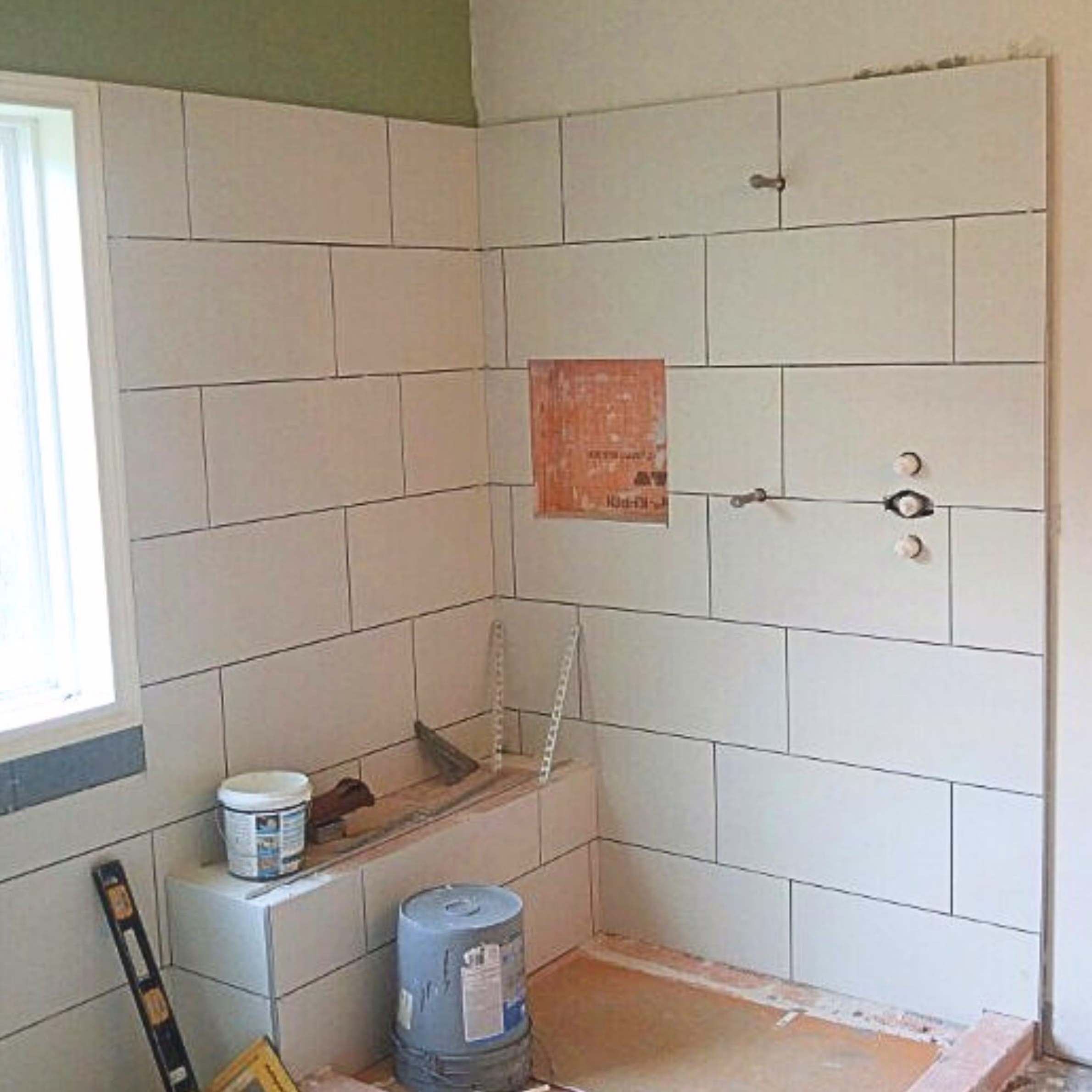 Large rectangular wall tiles being installed around a shower during a bathroom remodel.