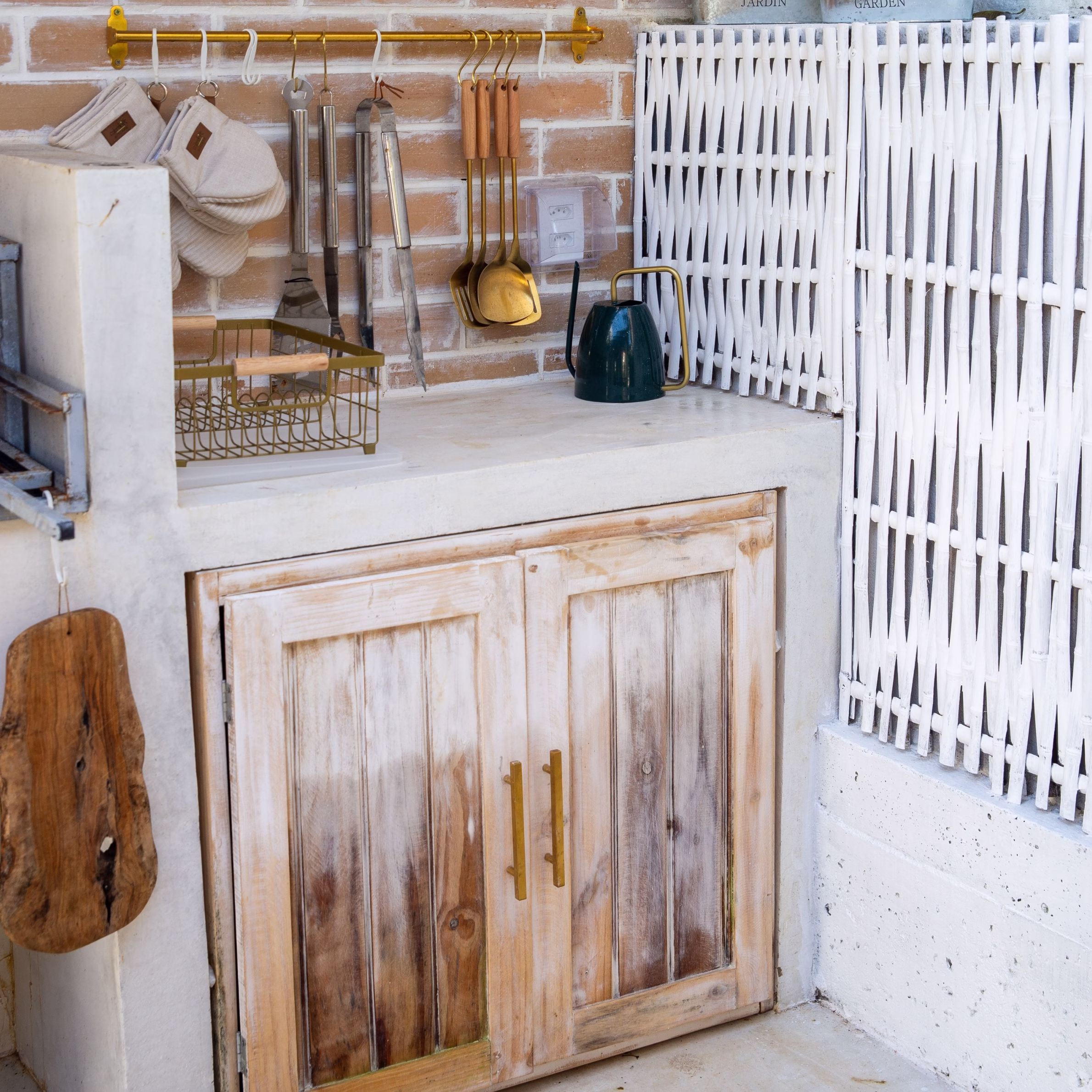 Outdoor kitchen counter with weathered wood cabinetry, hanging cooking utensils, and built-in storage.
