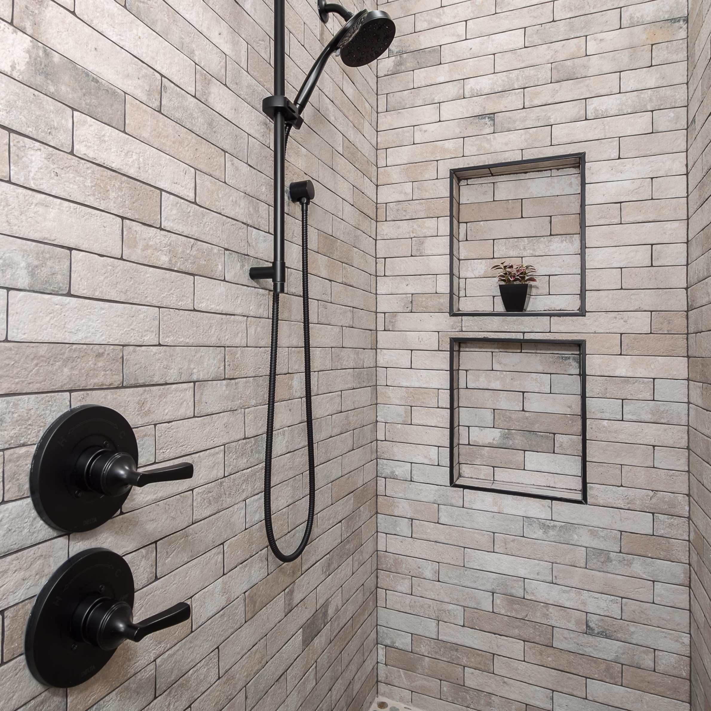 Walk-in shower with full-height rectangular tile, two black-trimmed wall niches, handheld shower fixture, and matte black controls.