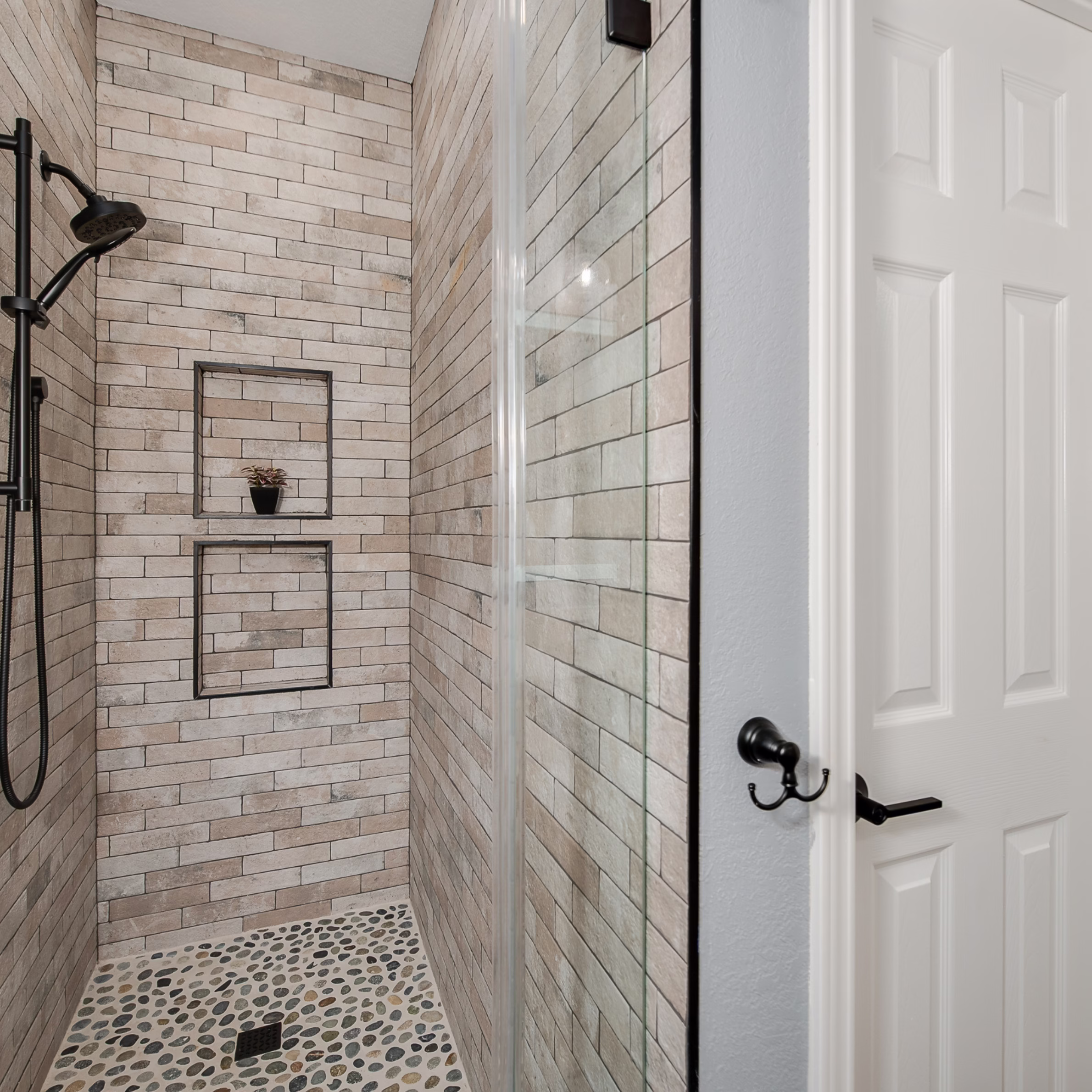 Remodeled guest bathroom walk-in shower with glass enclosure, full-height tile, pebble floor, and stacked wall niches.