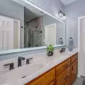 Retained oak double vanity updated with matte black hardware and faucets beneath a large illuminated mirror.