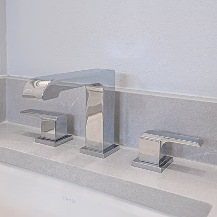 Close-up of the updated chrome Kohler faucet and gray quartz countertop in the remodeled bathroom.