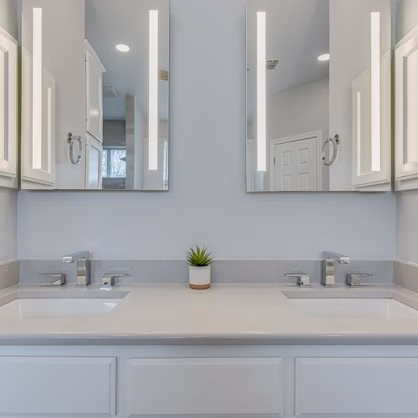Remodeled double vanity with quartz countertop, rectangular sinks, chrome fixtures and individual lighted mirrors.