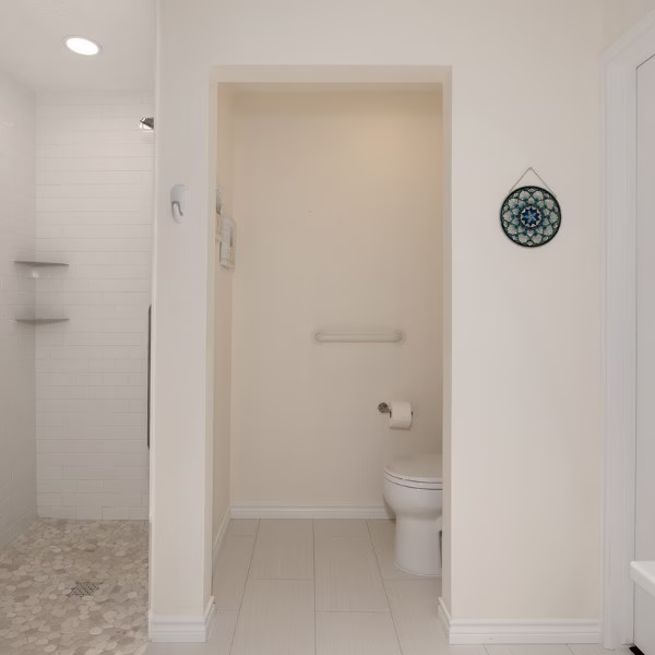 Remodeled water closet with grab bar and open layout connected to the new curbless primary shower.