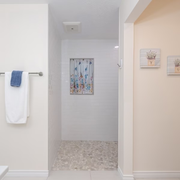 Spacious curbless shower with pebble tile flooring and white subway tile designed for long-term accessibility.