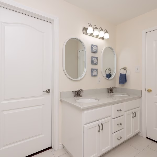 Remodeled primary bathroom vanity with painted cabinets, quartz countertop, double sinks, and updated lighting.