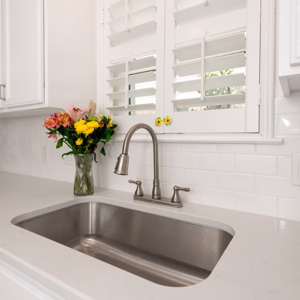 Updated kitchen sink with white quartz countertops, white subway tile backsplash, and plantation shutters.
