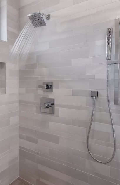 Walk-in shower with gray tile, modern rain shower head and handheld shower mounted on an adjustable slider bar.