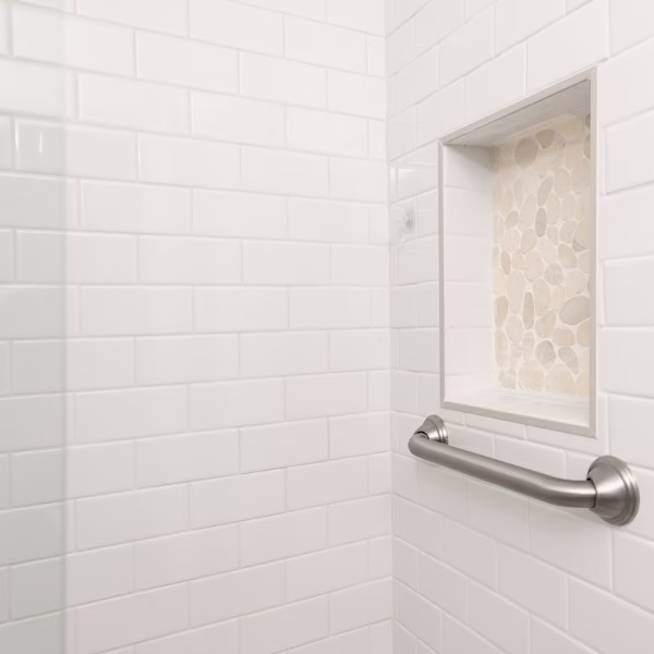 Close-up of recessed shower niche with pebble tile accent and stainless steel grab bar in the remodeled primary bathroom.