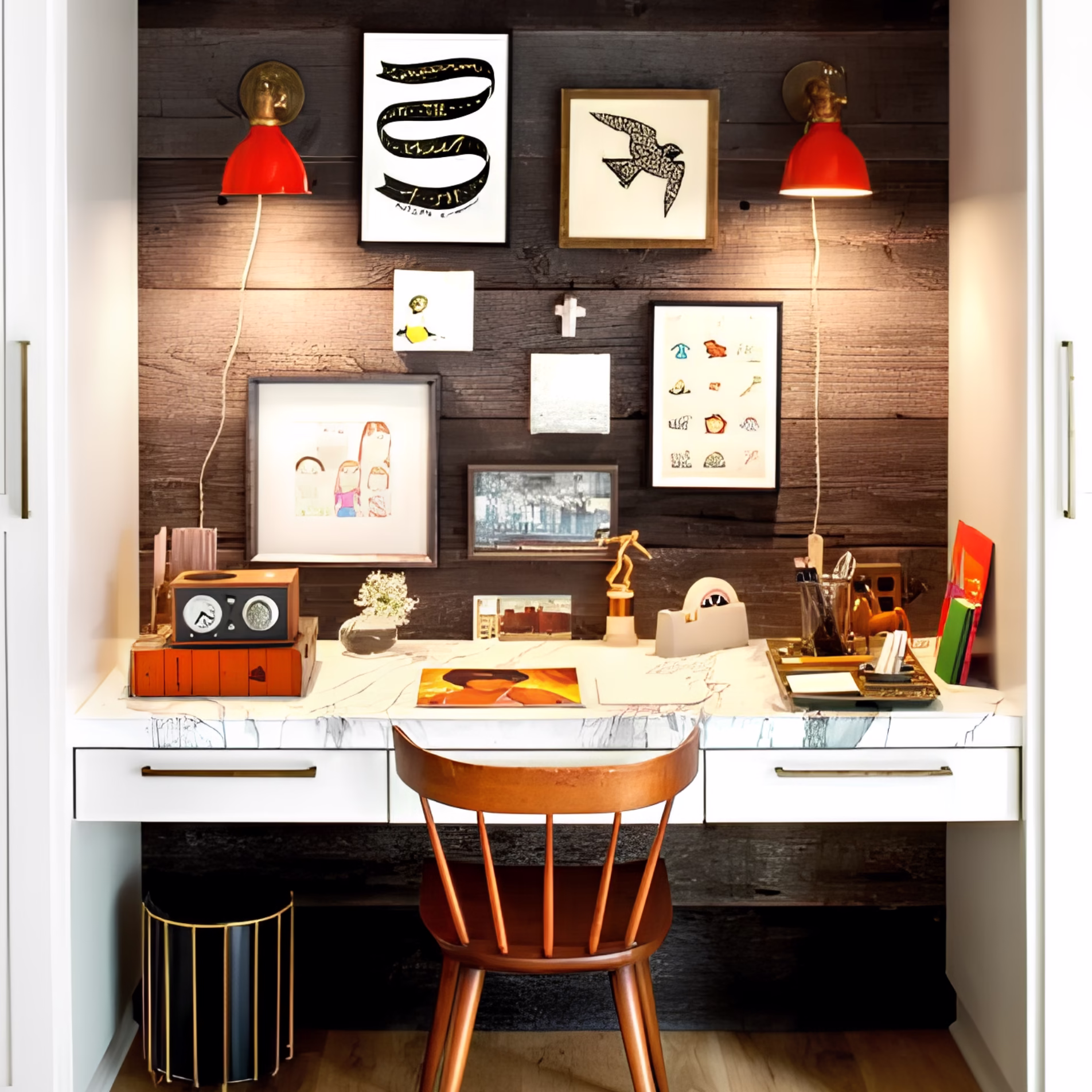 Compact built-in desk nook with a dark wood accent wall, white cabinetry, red wall sconces, and framed artwork.