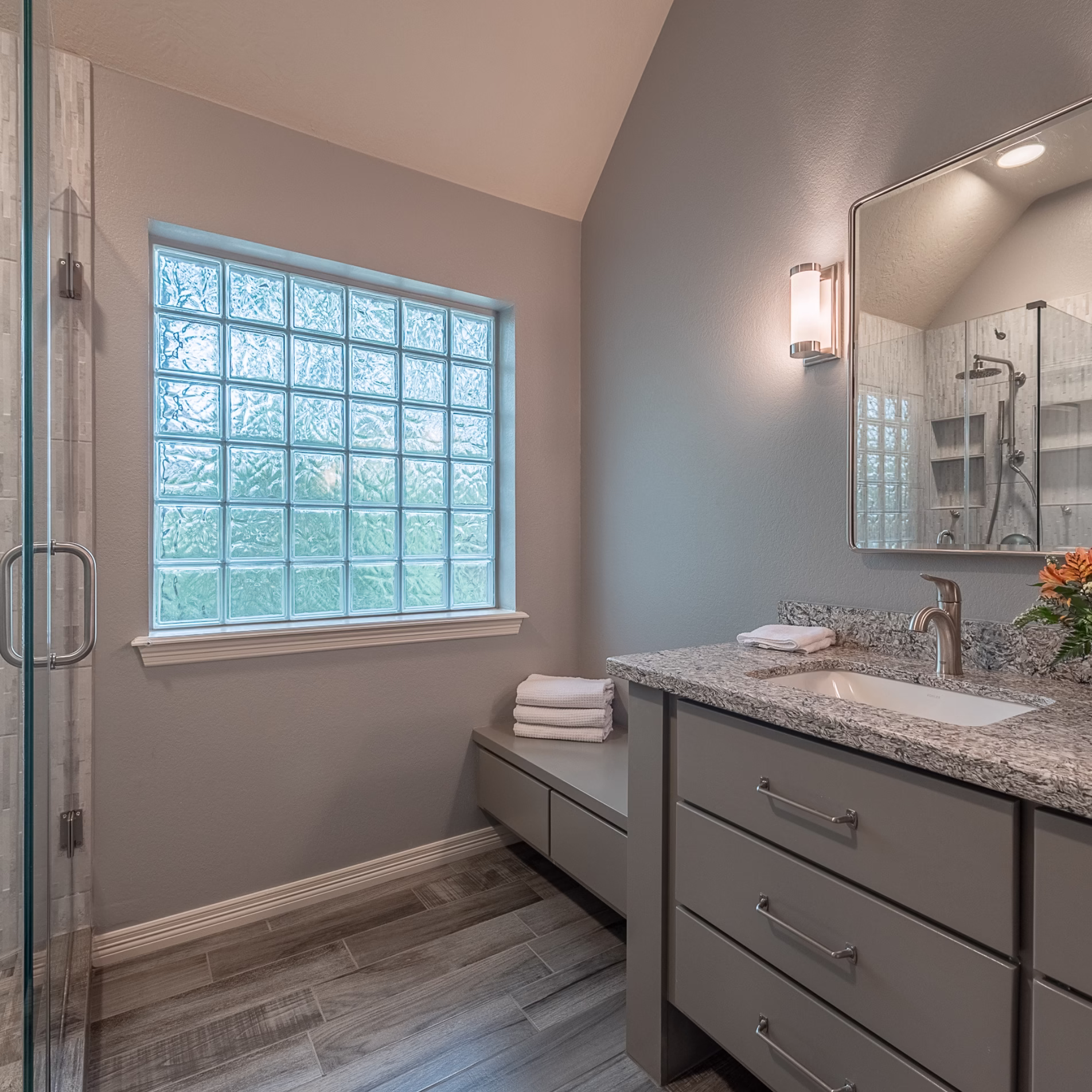 Remodeled primary bathroom with the former bathtub area replaced by an open floor area and built-in bench beneath a glass block window.