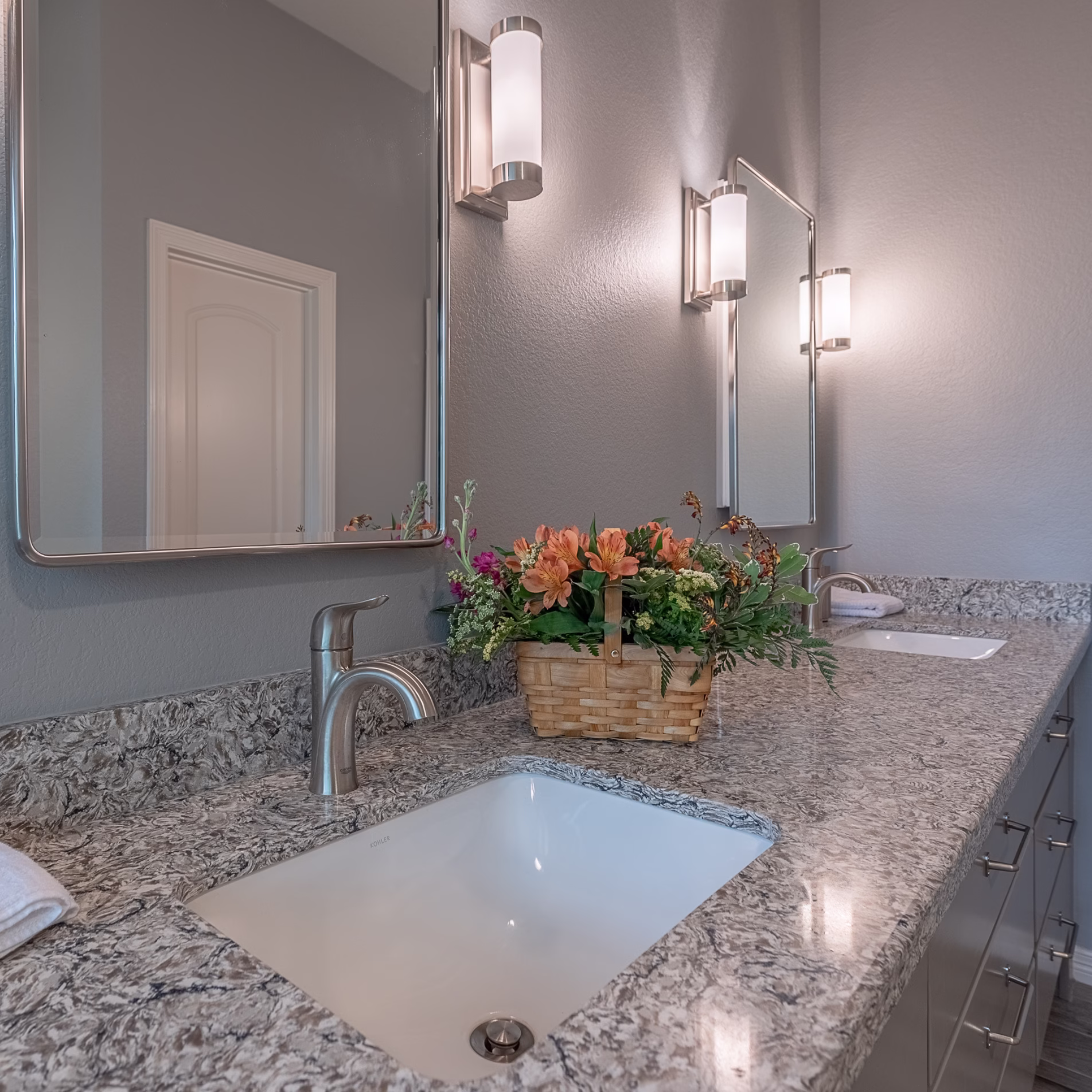 Remodeled bathroom vanity with stone countertop, undermount sink, brushed metal faucet, individual mirror, and wall sconces.