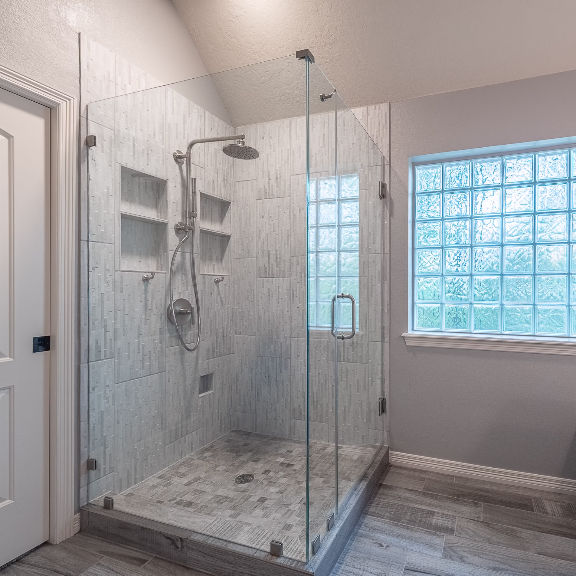 Expanded tiled shower after remodeling with a frameless glass enclosure and opening oriented toward the opposite side.