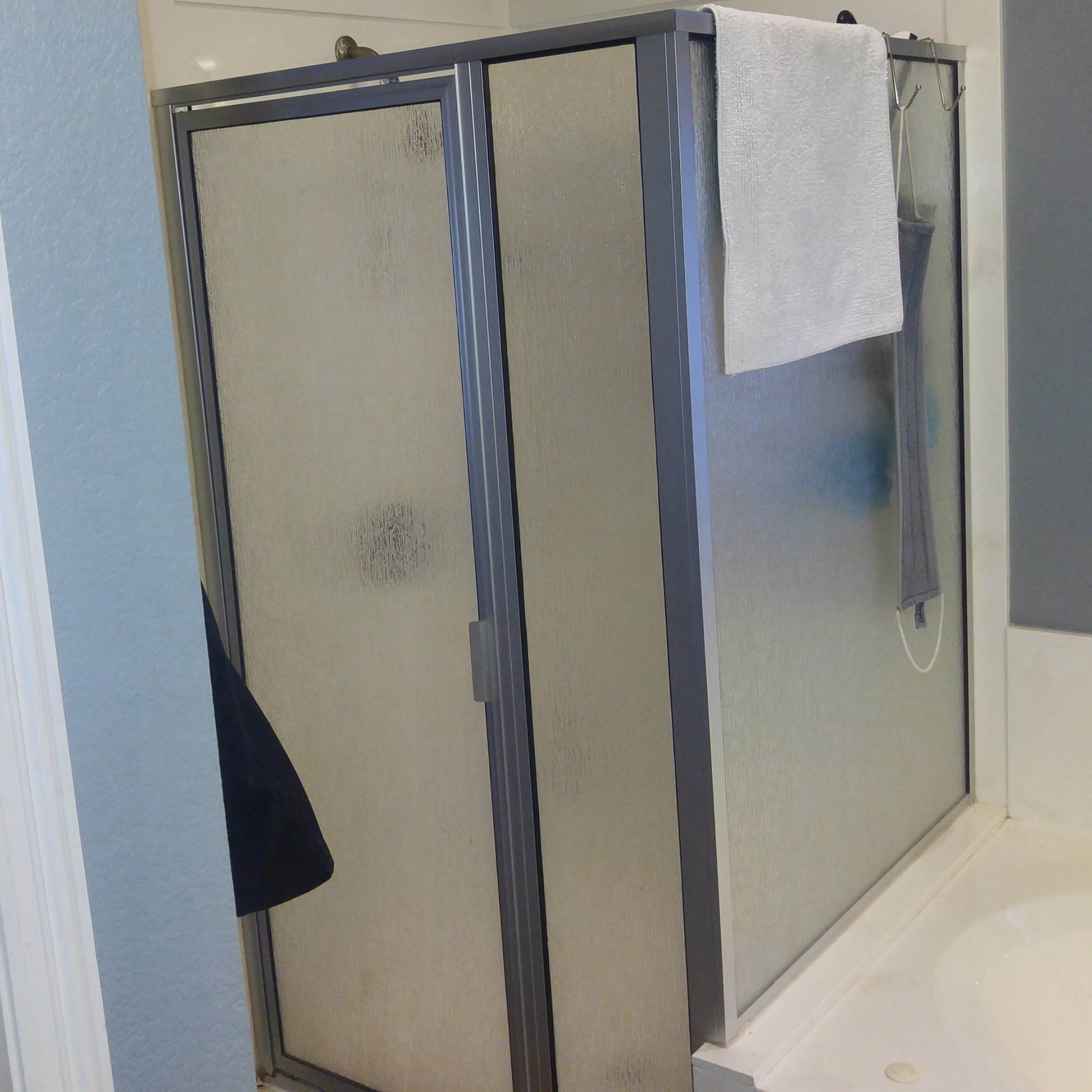 Original compact shower with framed textured glass enclosure beside the bathtub.