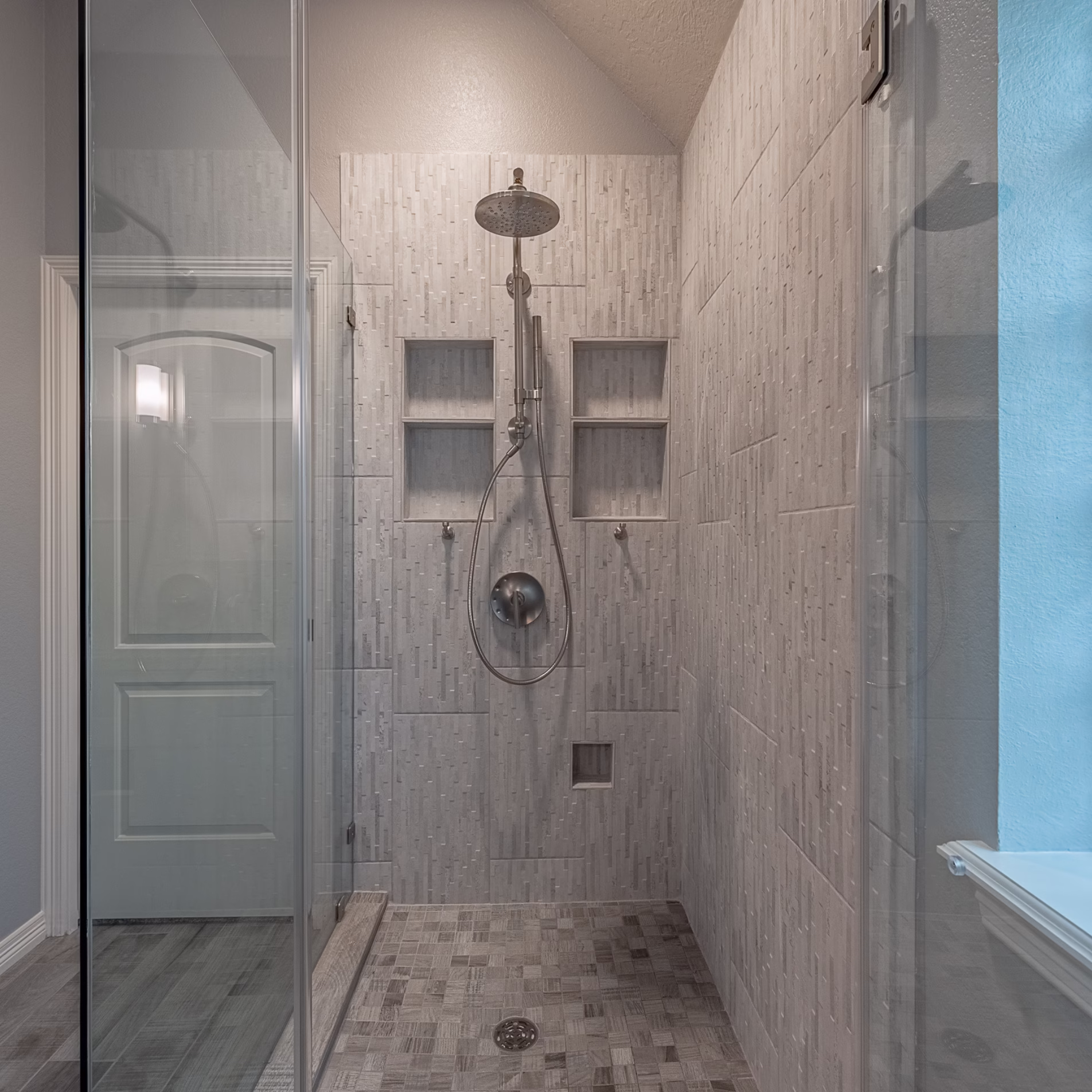 Interior view of the expanded shower with tiled walls and floor, built-in niches, rainfall showerhead, and handheld fixture.