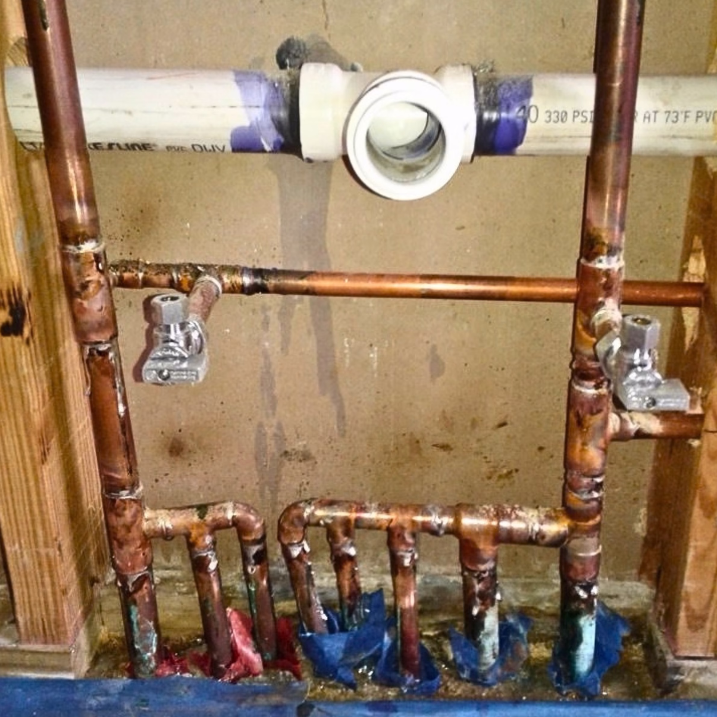 Exposed copper plumbing and PVC drain lines during repairs inside a wall during a home remodel.
