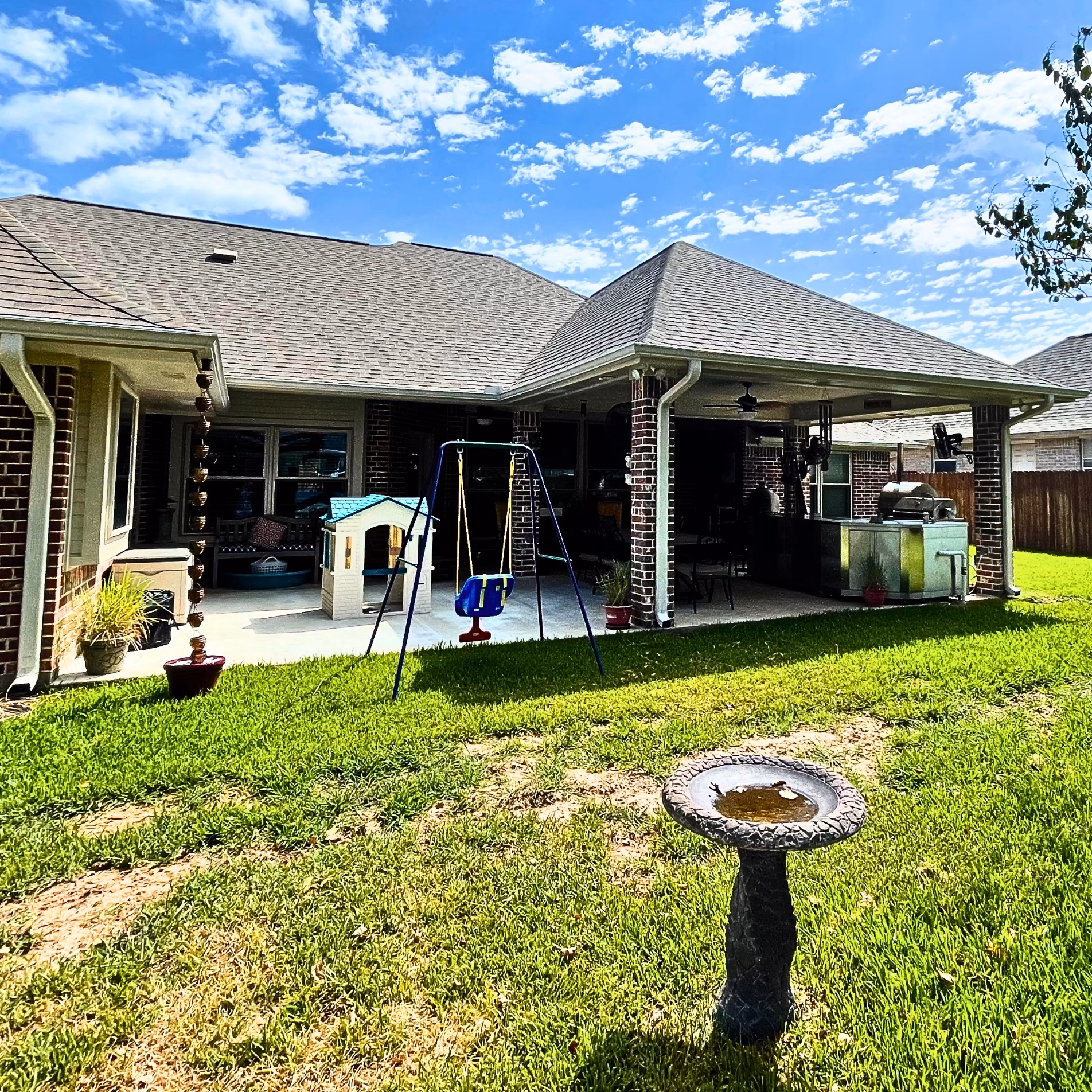 Wide backyard view of the completed Edelweiss Estates patio addition with an extended roof, brick columns, and outdoor cooking area.