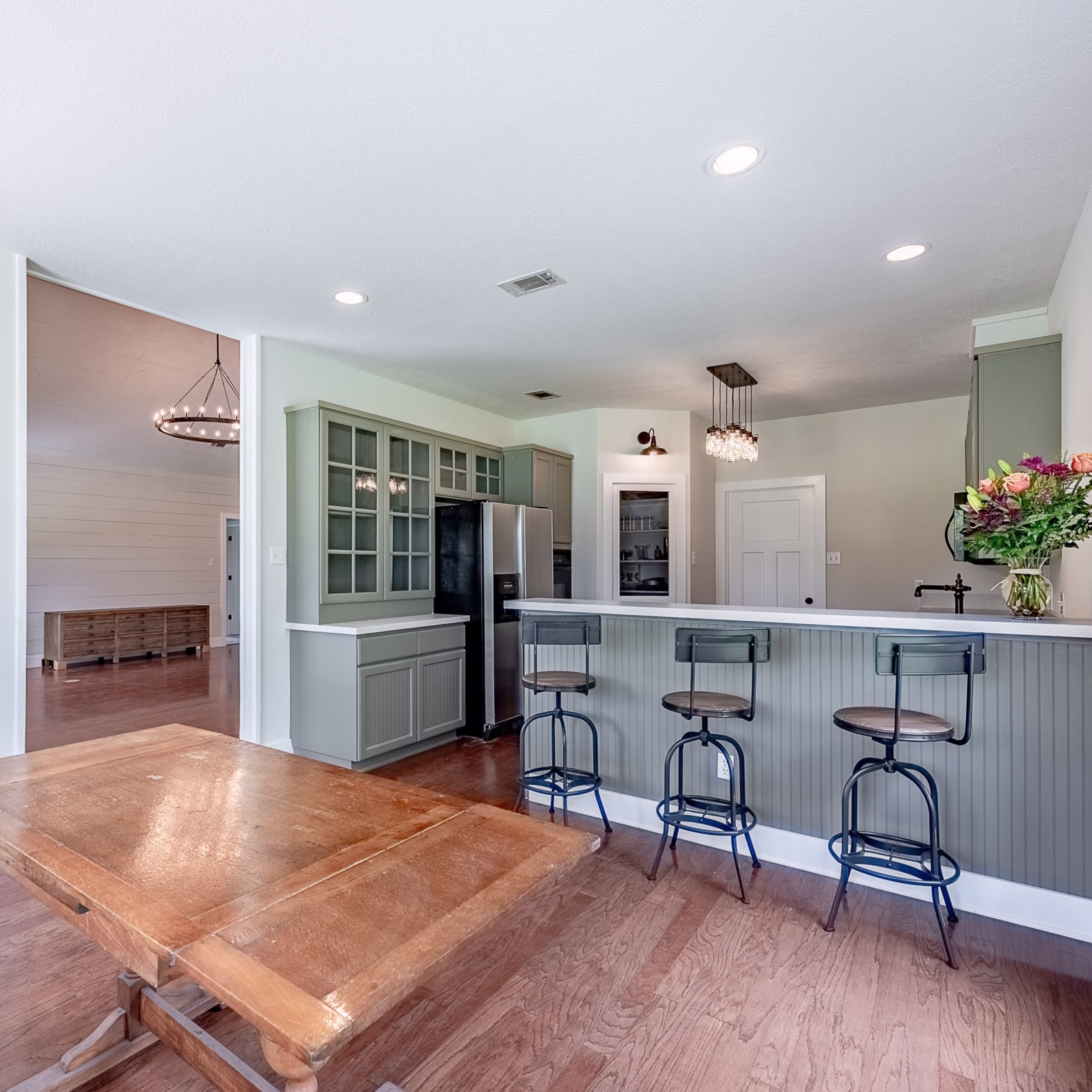 Finished open kitchen and dining space with green cabinetry, wood flooring, and a large wood dining table after remodeling.