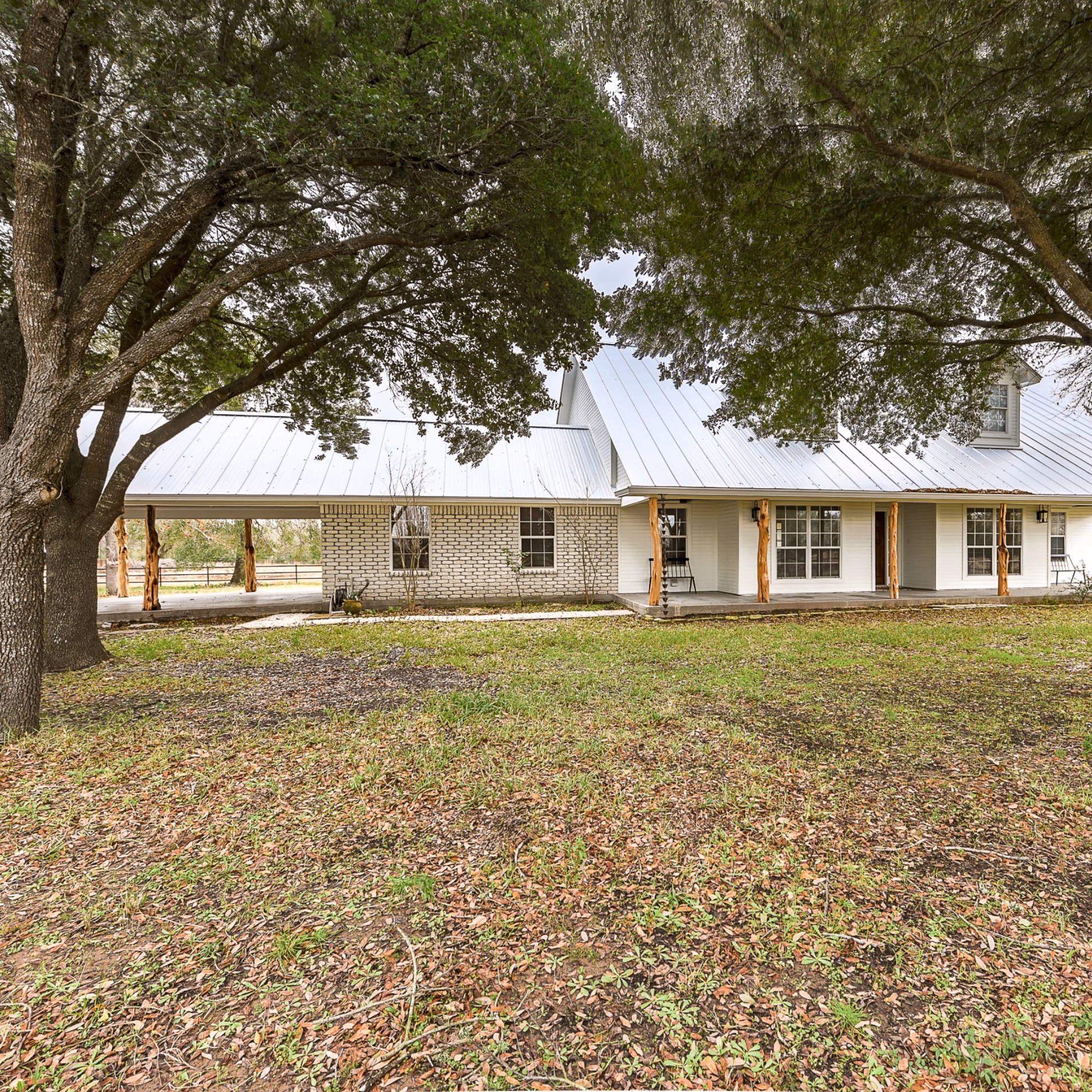 Newly constructed home with gray siding and white trim surrounded by existing mature trees across the front lawn.