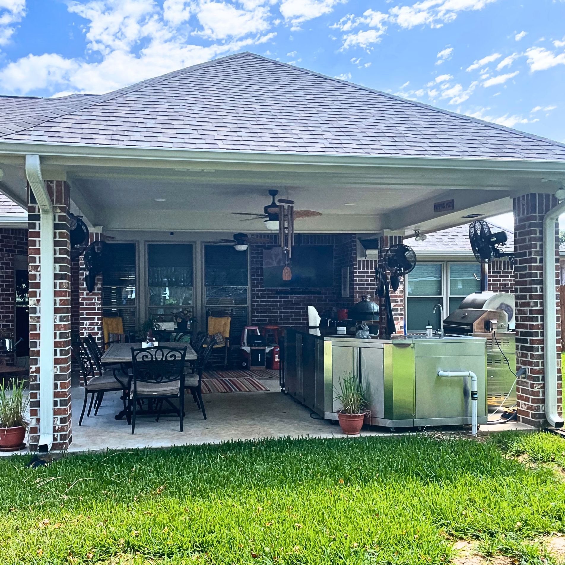 Expanded covered patio in Edelweiss Estates with matching brick columns, a new roof extension, dining area, and outdoor kitchen equipment.