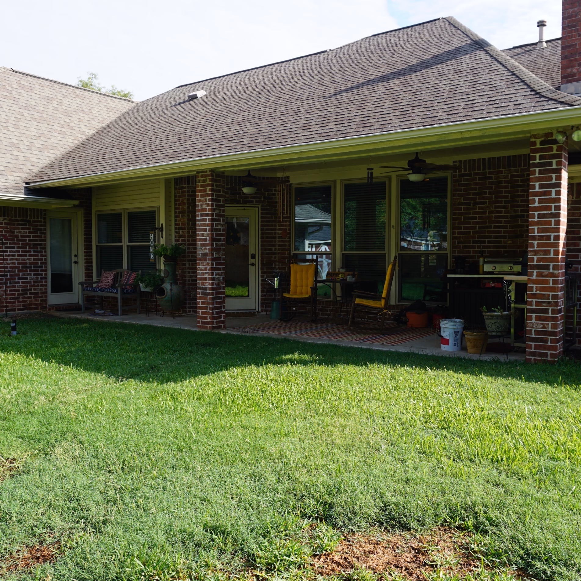 Original covered patio before expansion, showing a narrow concrete seating area, brick columns, and a grill beside the backyard.