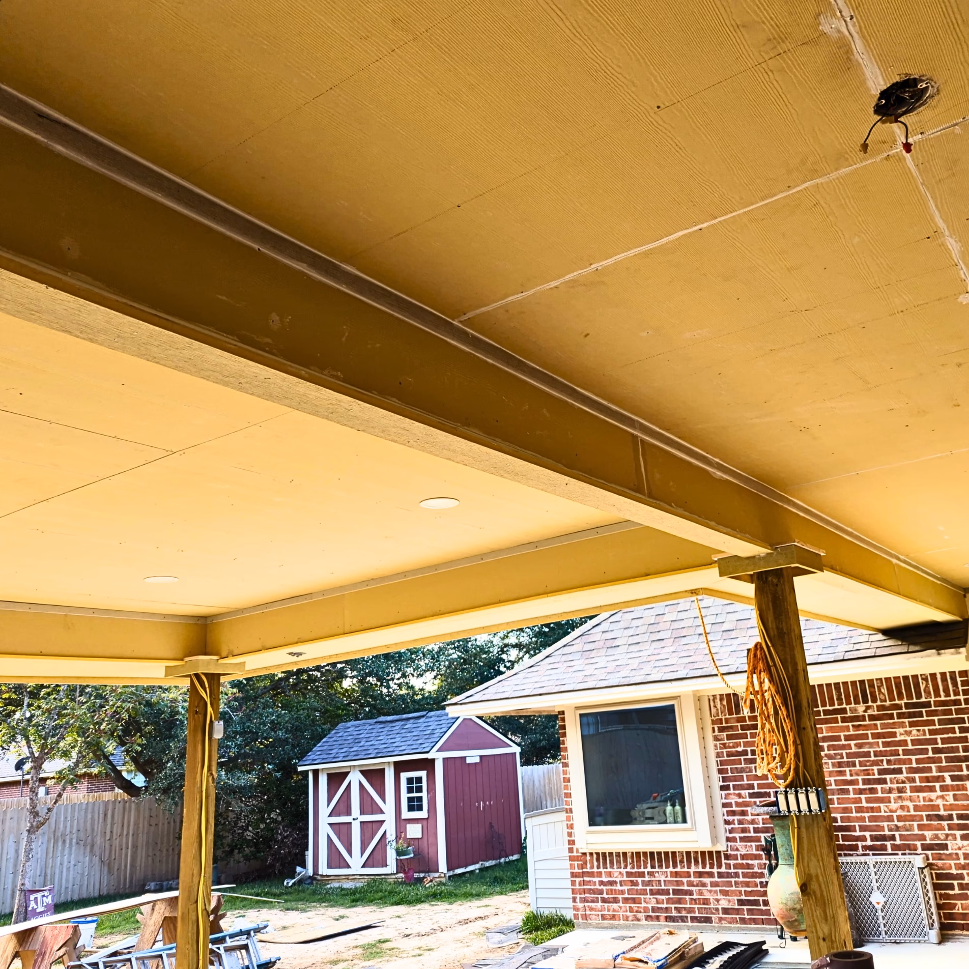 Flat ceiling and recessed lights beneath the covered patio addition during construction, with exposed support posts and beams.