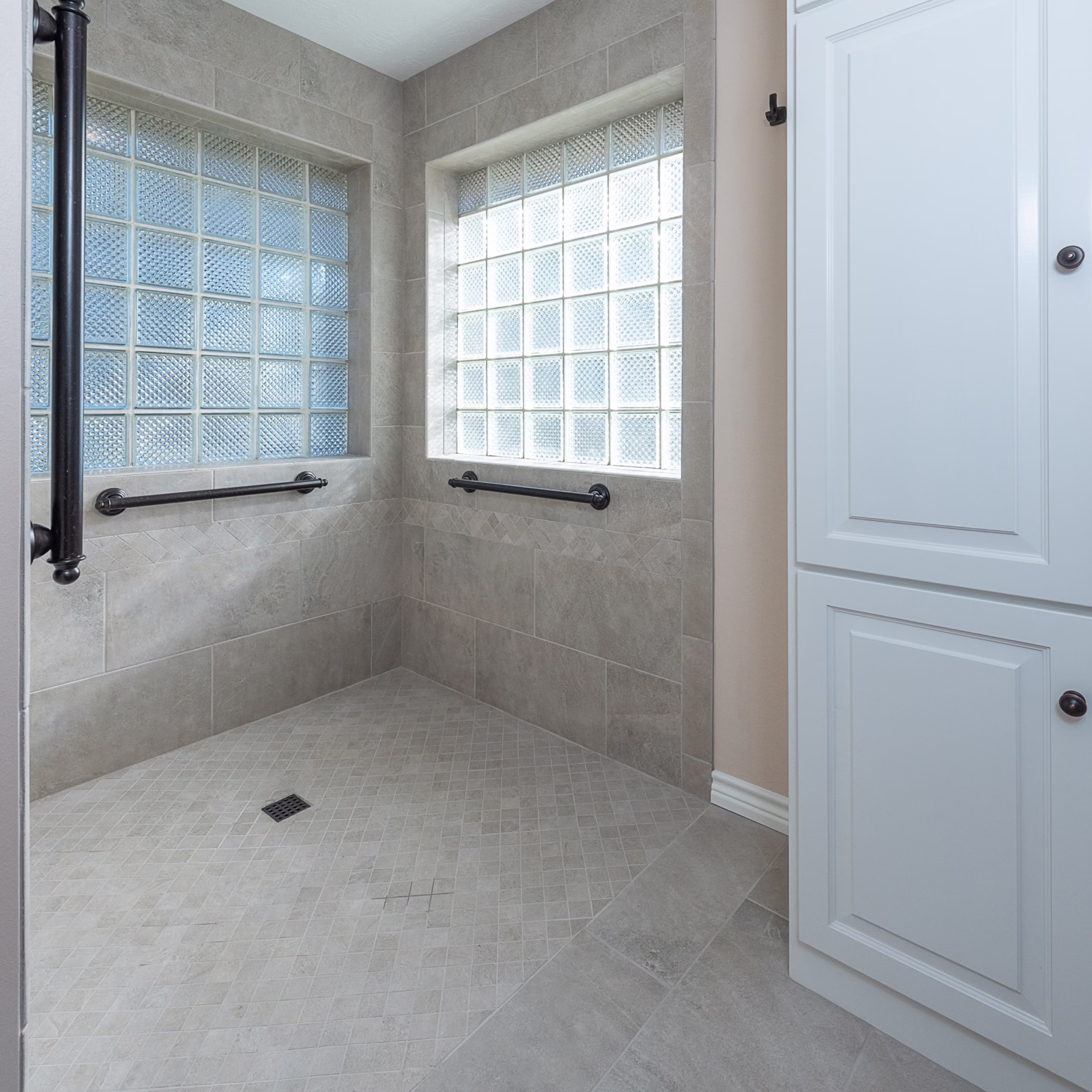 Accessible roll-in shower with a low-threshold entrance, tiled walls, built-in grab bars, and glass block windows.