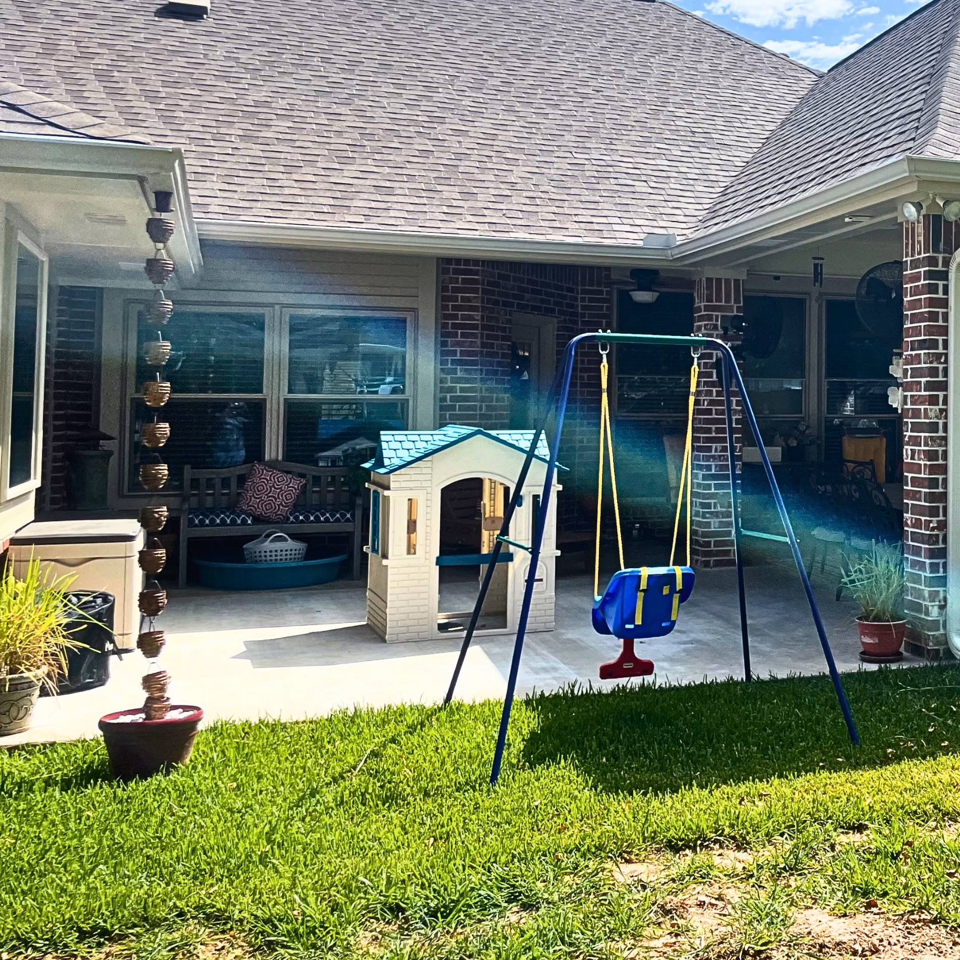 Expanded concrete patio and covered outdoor entertaining area with a children's playhouse and swing set beside the backyard lawn.