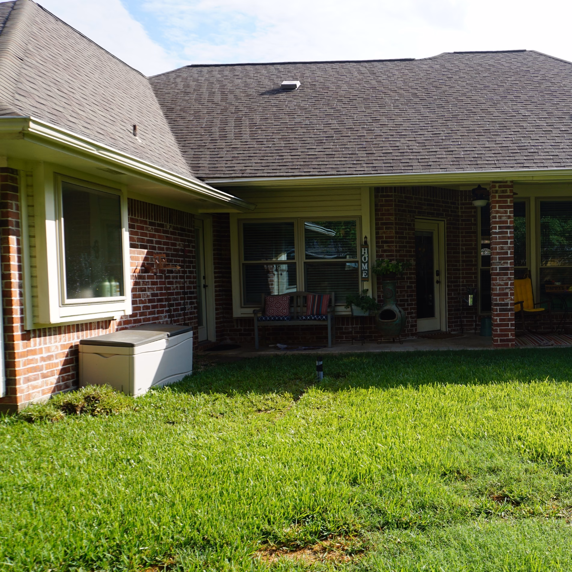 Original covered patio and backyard before the addition, featuring brick columns, a small seating area, and surrounding lawn.