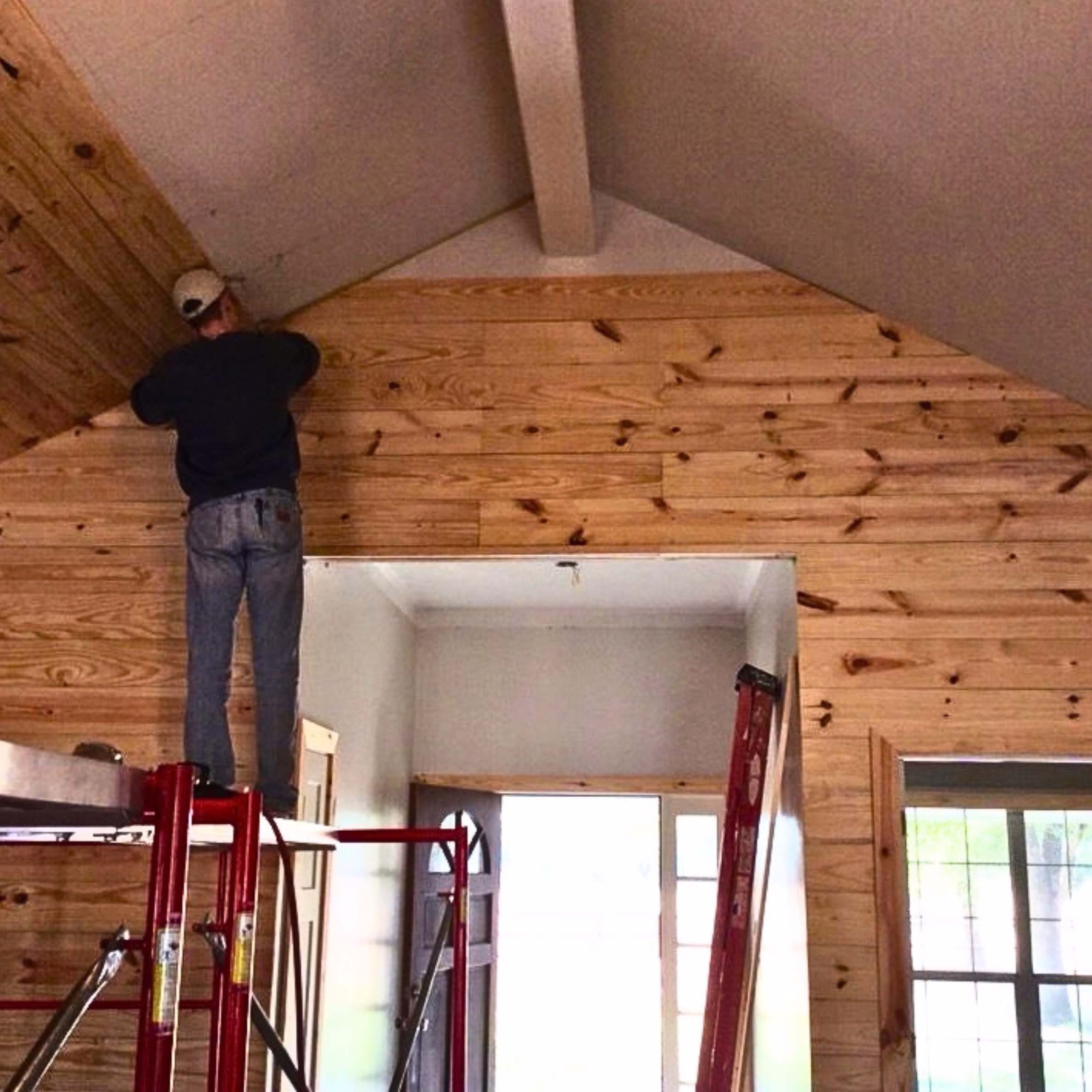Carpenter installing natural wood wall planks during the construction phase of a home remodel.